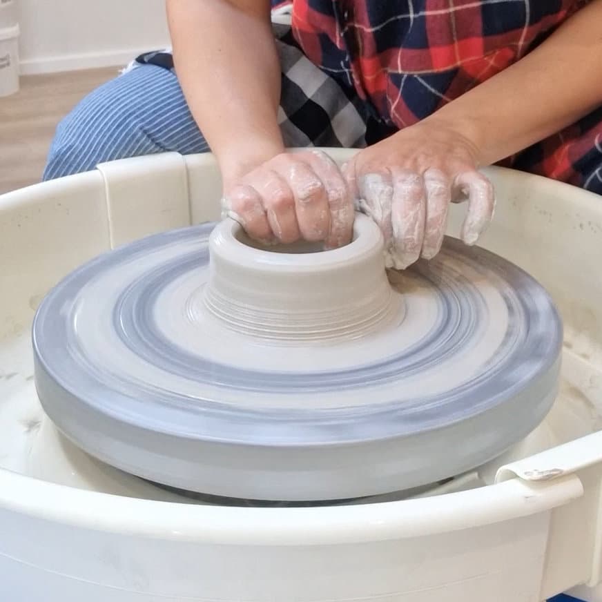 Hands shaping clay on a pottery wheel