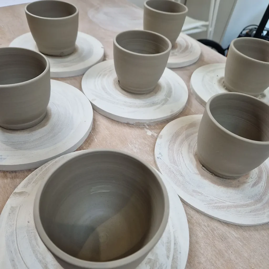 Freshly thrown ceramic mugs drying on a wooden board at Anat Handmade Pottery.