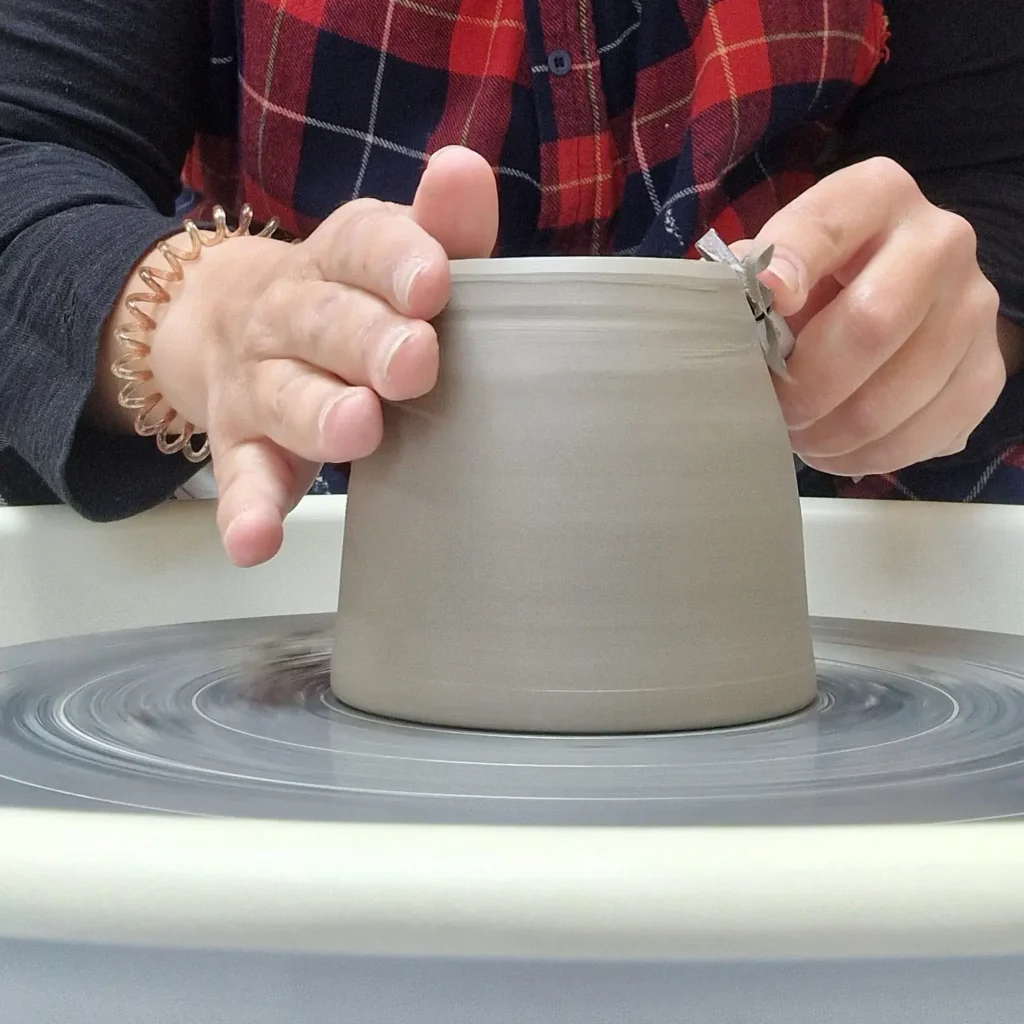 Anat trimming the base of a leather-hard ceramic mug on the potter's wheel.