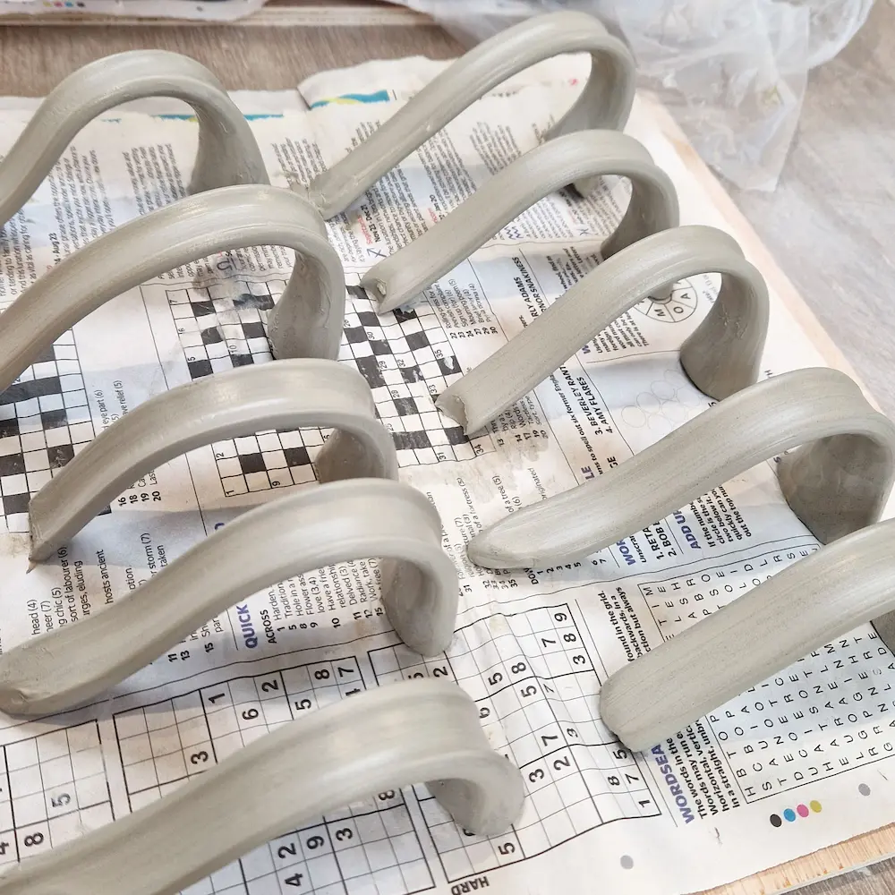 Hand-pulled clay handles resting on a studio workbench before being attached to mugs.