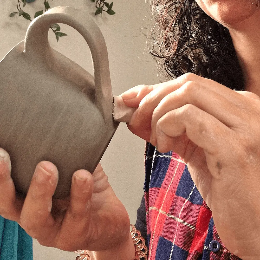 Attaching a handmade clay handle to a ceramic mug.